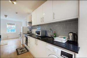 uma cozinha com armários brancos e um balcão preto em New Spacious 1 bed studio flat in Aldgate em Londres