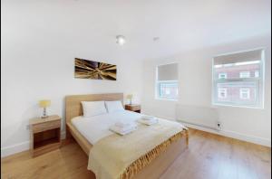 a white bedroom with a bed and two windows at Modern split level 1 bedroom flat in Aldgate in London