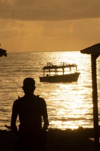 una persona seduta sulla spiaggia con una barca in acqua di Billionaire Resort & Retreat Malindi a Malindi