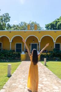 une femme en robe jaune debout devant un bâtiment jaune dans l'établissement Hacienda San Miguel Yucatan, à Valladolid
