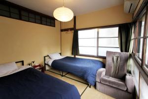 a bedroom with two beds and a chair and a window at Roku Hostel Hiroshima in Hiroshima
