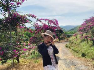 Eine Frau mit einem Hut, die auf einer unbefestigten Straße mit Blumen steht. in der Unterkunft FOREST BREATH ECO-LODGE in Tân Phú