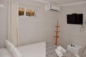 a white bedroom with a bed and a tv on the wall at Pousada da Divisa in Tamandaré