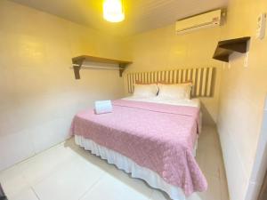 um pequeno quarto com uma cama com um cobertor rosa em FLAT BAÍA DO SANCHO em Fernando de Noronha