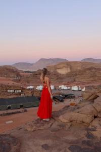 una mujer con un vestido rojo de pie en algunas rocas en Mazayen Rum Camp en Wadi Rum