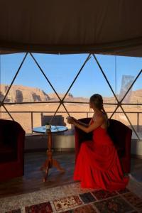 a woman in a red dress sitting in a room with a view at Mazayen Rum Camp in Wadi Rum