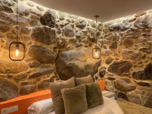 1 dormitorio con una pared de piedra, cama y luces en As Penedas, Casa dos Arcos, en Sober