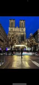 uma pessoa andando em frente a uma catedral com luzes de Natal em Hôtel De La Cathédrale em Reims