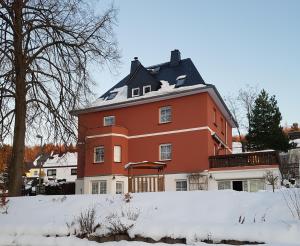 uma grande casa vermelha com neve no telhado em Pension Irmisch em Aue