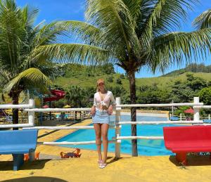 a woman standing next to a fence next to a pool at Tijota Hotel Fazenda in Ipatinga