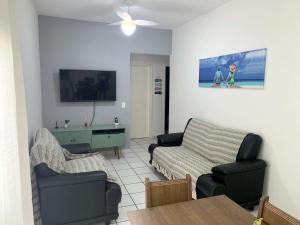 ein Wohnzimmer mit einem Sofa, Stühlen und einem TV in der Unterkunft Apartamento aconchegante - Enseada - Guarujá in Guarujá