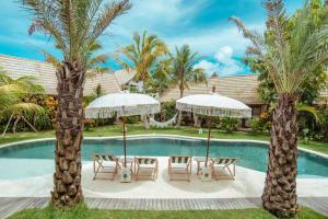 a resort pool with chairs and umbrellas and palm trees at Mule Malu Tropical Stay in Uluwatu