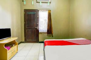 Cette chambre comprend un lit, une télévision et une porte. dans l'établissement Super OYO 1I3676 Wisma Al-fahmi Syariah, à Maniskaler