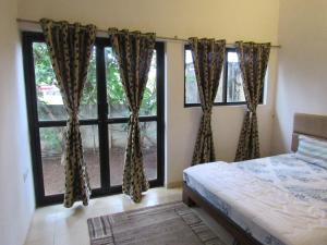 sypialnia z łóżkiem i dwoma dużymi oknami w obiekcie Retreat Holiday Homes, Twin Chalets at Sparsh Resorts and Chalets, Karjat w mieście Karjat