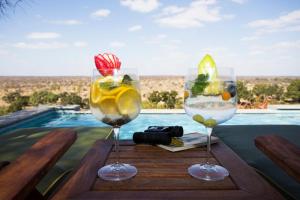 dois copos de vinho sentados numa mesa ao lado de uma piscina em Klaserie Drift em Klaserie Private Nature Reserve