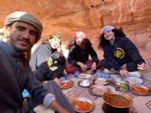 grupa ludzi siedzących przy stole jedzących jedzenie w obiekcie Wadi Rum Cave Camp &Jeep Tour w mieście Wadi Rum