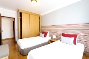 a hotel room with two beds with red pillows at Milfontes Private Homes - Duna Parque Group in Vila Nova de Milfontes