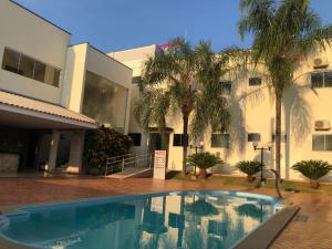 a swimming pool in front of a building with palm trees at Hotel Baeza in Goiatuba