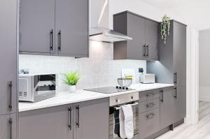a kitchen with white and gray cabinets and a microwave at Caemawr Place - Stylish Home TV in Every Bedroom! in Swansea