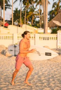 a man walking on the beach with a surfboard at Hotelito Los Sueños in Sayulita