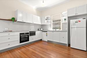 cocina blanca con electrodomésticos blancos y suelo de madera en Wambiri on Lighthouse Road en Byron Bay