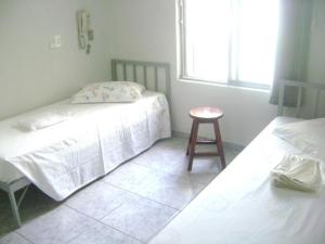 two beds in a room with a stool and a window at Hotel Arbom in Mogi-Guaçu