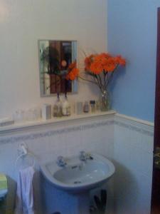 La salle de bains est pourvue d'un lavabo et d'un vase avec des fleurs orange. dans l'établissement Newcourt B & B, à Llantwit Major
