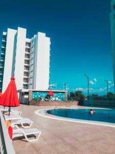 une piscine avec des chaises et un parasol rouge, ainsi que certains bâtiments dans l'établissement Apto Alquiler Girardot, à Girardot