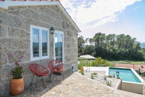 a stone house with a swimming pool and two red chairs at Casa Monte do Cervo in Vila Nova de Cerveira