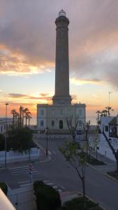 a lighthouse in front of a building with a sunset at Remarkable 3-Bed Apartment in Chipiona in Chipiona