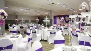 a banquet hall with white tables and purple chairs at Merit Hotel & Suites in Fort McMurray