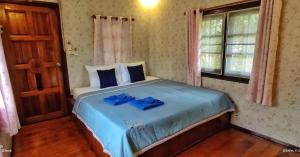 a bedroom with a bed with blue sheets and a window at TA YAI HOMESTAY (ตา ยาย โฮมสเตย์) in Ko Kood