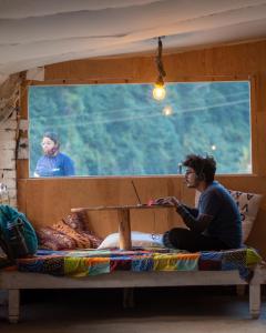 un hombre sentado en una cama frente a una ventana en Young Monk Hostel & Cafe Old Manali, en Manali