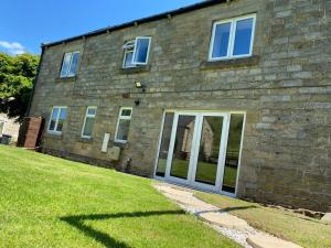 a brick house with doors and a grass yard at Delightful stone barn, with superb views, Ramsgill in Pateley Bridge