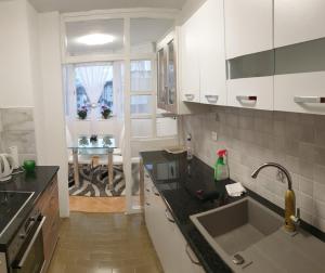 eine Küche mit weißen Schränken, einer Spüle und einem Tisch in der Unterkunft Apartman Hana in Sanski most