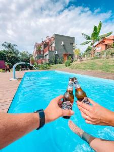 dos personas sosteniendo botellas de cerveza frente a una piscina en Reserva Brasileira, en Praia do Rosa
