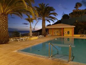 a swimming pool with palm trees and a building at Hotel Cais da Oliveira in Caniço