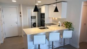 una cocina con armarios blancos y una isla con taburetes. en Apartamento 1º Línea de Playa - Duna Beach, en Torrox Costa
