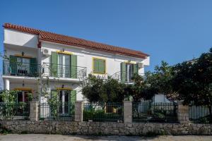 a white house with green windows and a stone wall at Penelope - LOGGOS APARTMENTS in Longós
