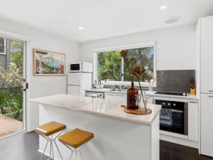 a white kitchen with a counter and two stools at Point Roadknight Paradise Villa 6 in Anglesea