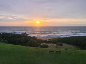 un tramonto sull'oceano con due panchine in un campo di Rockview Holiday Beach Apartment a Hibberdene Altre 4 foto