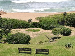 two benches sitting on the grass near a beach at Rockview Holiday Beach Apartment in Hibberdene