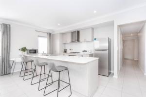 a white kitchen with a white counter and bar stools at The Kingsley’s Place - EXECUTIVE ESCAPES in Perth