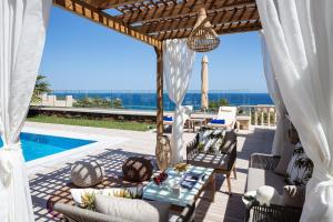 un patio con mesa, sillas y piscina en Agapi Villas I & II, fairytale seaside retreats, By ThinkVilla, en Panormos Rethymno