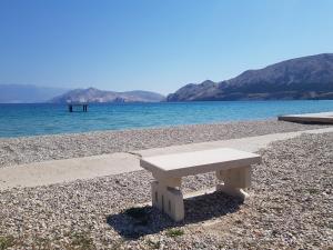 a white bench sitting on a beach next to the water at Apartments Mrkus in Baška