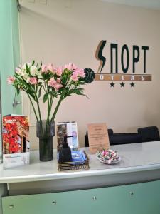 a table with a vase of pink flowers and books at Sport-Hotel in Tomsk