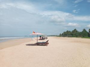 a beach with a bench and an umbrella on the sand at Tharul Home in Bentota