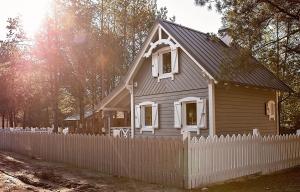 a small house behind a white picket fence at Leśna Osada na Kaszubach - drewniane domy na wynajem in Bartoszylas