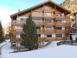 un gran edificio de apartamentos con un árbol en la nieve en Apartment Select by Interhome, en Zermatt
