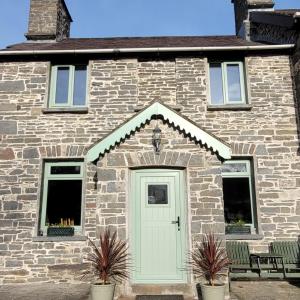 a stone house with a green door and two chairs at Mill Cottage in Llanddeiniol